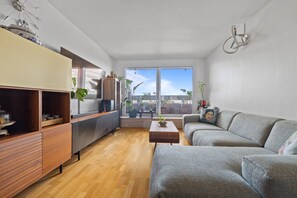 A modern living room with a sofa, a coffee table, and a TV stand. There are plants and a view of the sky through large windows. - Attica, 3BR/2BA, 6 people (París)
