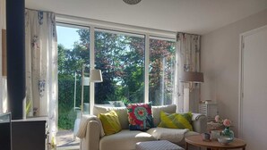 A living room with a sofa, ottoman, and a small round table with decorative items. - Bungalow "The Shrimp" close to the beach! Air conditioning! South corner 1 (Renesse)