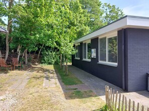 A modern house with a dark exterior, large windows, and a paved pathway leading to a wooden deck.