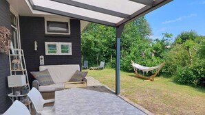 A patio with a table, chairs, a hammock, and a black wall with framed pictures. - Bungalow "The Shrimp" close to the beach! Air conditioning! South corner 1 (Renesse)