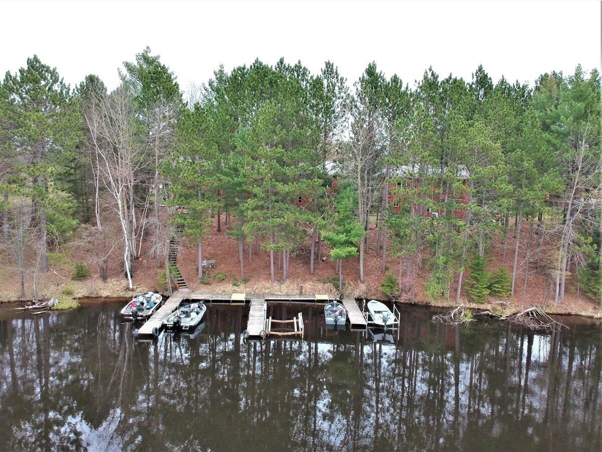 A dock with several boats, surrounded by a forested area with tall trees.