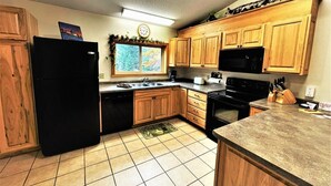 A kitchen with wooden cabinets, a black refrigerator, a microwave, and a stove. - Red Pines -  Elk Lake Condo #3 (Phillips)