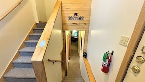 Eine Treppe mit Holzwandhandlauf, Teppichstufen, einem Willkommensschild, einem Feuerlöscher und einer Tür mit Schlüsselloch.