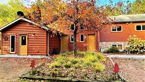 Eine Blockhütte mit einer Veranda, ein kleiner Garten mit einem Baum und eine Steinmauer.