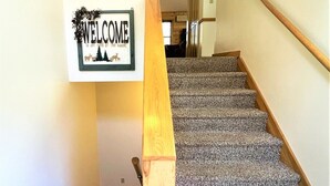 Eine Treppe mit Teppichstufen und einem hölzernen Geländer, die zu einem Raum mit einer Willkommensanzeige führt.