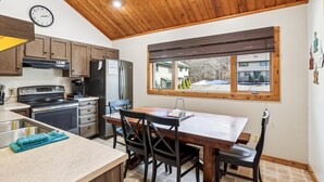 A kitchen with wooden cabinets, a stainless steel refrigerator, a stove, and a dining table with chairs. - Ready to ski? This is the place to be! Check out Ski Ride Inn!! (Canaan Valley)