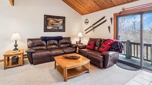 A cozy living room with a leather sofa, wooden coffee table, and a large window with a view of trees. - Ready to ski? This is the place to be! Check out Ski Ride Inn!! (Canaan Valley)