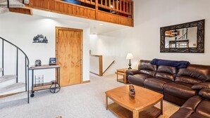 A spacious living room with a brown leather sofa, a wooden coffee table, a small side table with a lamp, a wooden door, and a staircase leading to a loft area. - Ready to ski? This is the place to be! Check out Ski Ride Inn!! (Canaan Valley)