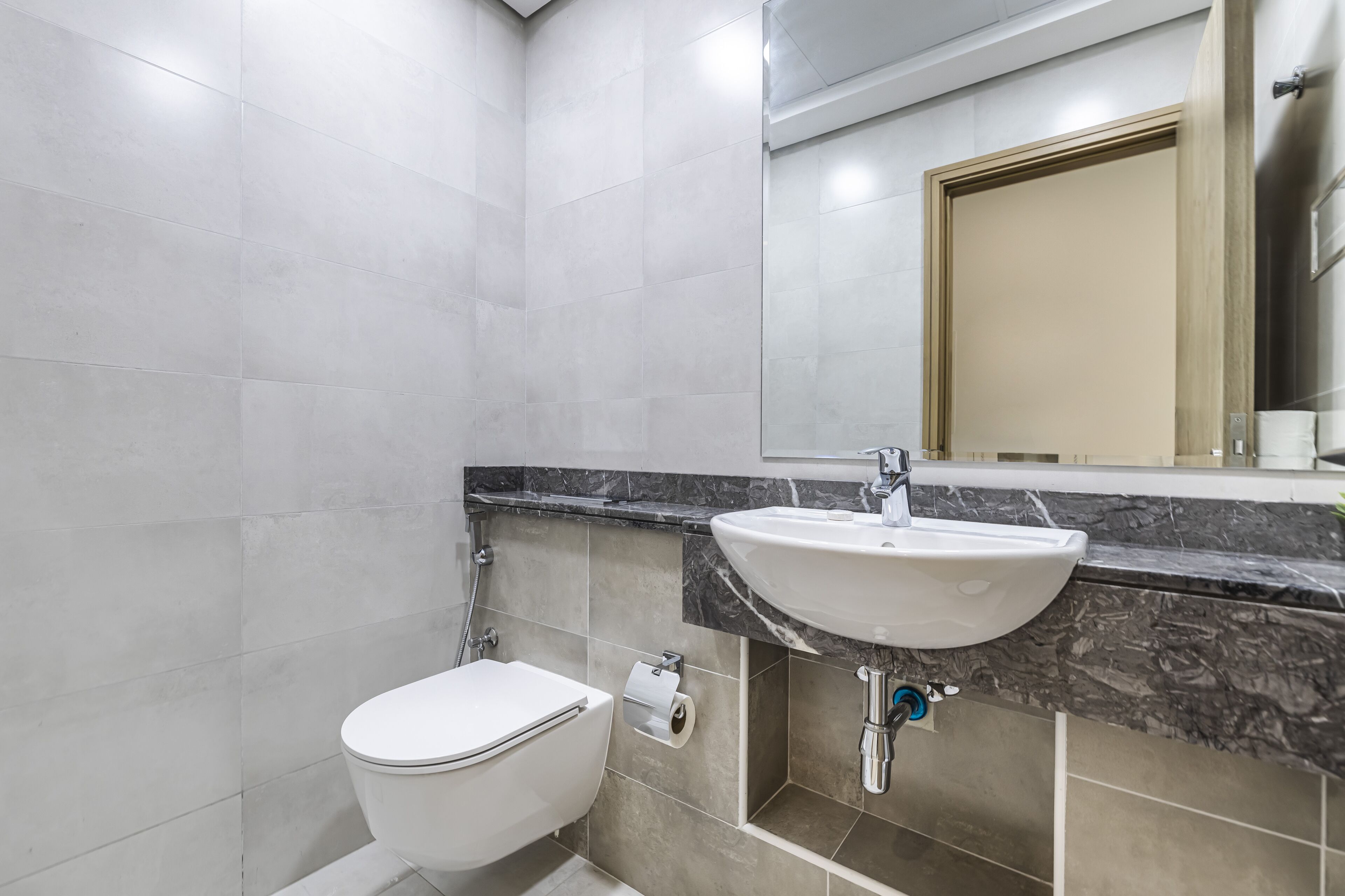 Een moderne badkamer met een wit toilet, een wastafel met een marmeren aanrechtblad en een spiegel boven de wastafel.