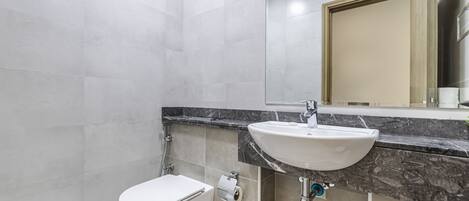 Een moderne badkamer met een wit toilet, een wastafel met een marmeren aanrechtblad en een spiegel boven de wastafel.