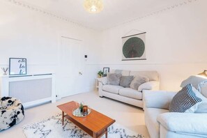Un salon moderne avec un canapé blanc, une table basse en bois et un pouf noir et blanc.