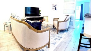 Ein Wohnzimmer mit Sofa, Sessel, Fernseher und Essbereich mit Tisch.
