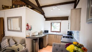 Una cocina compacta con estufa, microondas y lavabo. Hay una mesa de comedor con sillas, un sofá y un jarrón con flores.