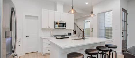 A modern kitchen with white cabinetry, a central island with stools, stainless steel appliances, and pendant lighting.