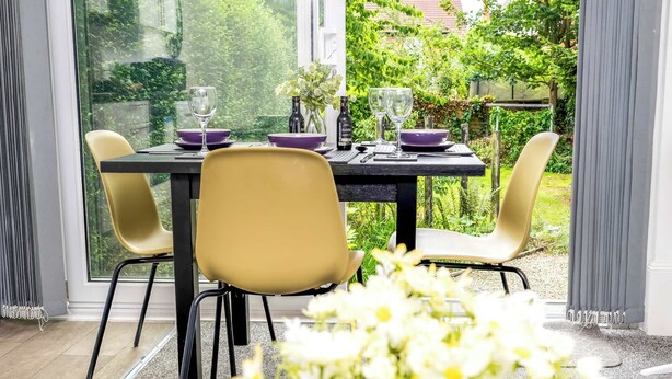A dining area with a table set for two, chairs, and a view of a garden through large windows. - Amethyst Suite Moseley Birmingham STAE-Homes (Birmingham)