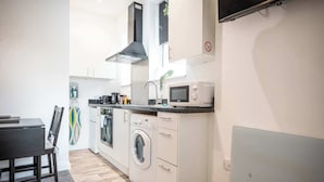 Cocina compacta con lavadora, microondas y comedor con mesa y sillas.