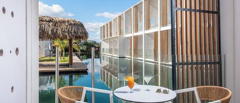 A balcony with a pool, white chairs, and a table with drinks.