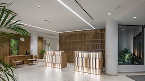 A modern reception area with a wooden reception desk, two seating areas, a large vertical wooden panel wall, and a large window with a view of greenery. - Sensus Experience by Lavris  (Hersonissos)