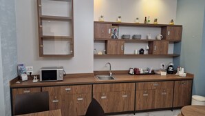Une cuisine moderne avec des meubles en bois, un four à micro-ondes et un évier. On y trouve des étagères remplies de divers objets, ainsi qu’une petite table avec des chaises.