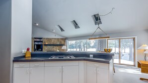A modern kitchen with white cabinets, a black countertop, and a built-in stove. There is a bookshelf with books and a small table with a lamp. - REDC23 - Spacious Home, Gas Fireplace, Ping Pong (Sunriver)