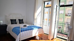 Una camera da letto con un letto, un comodino, una finestra vista edifici e una porta.
