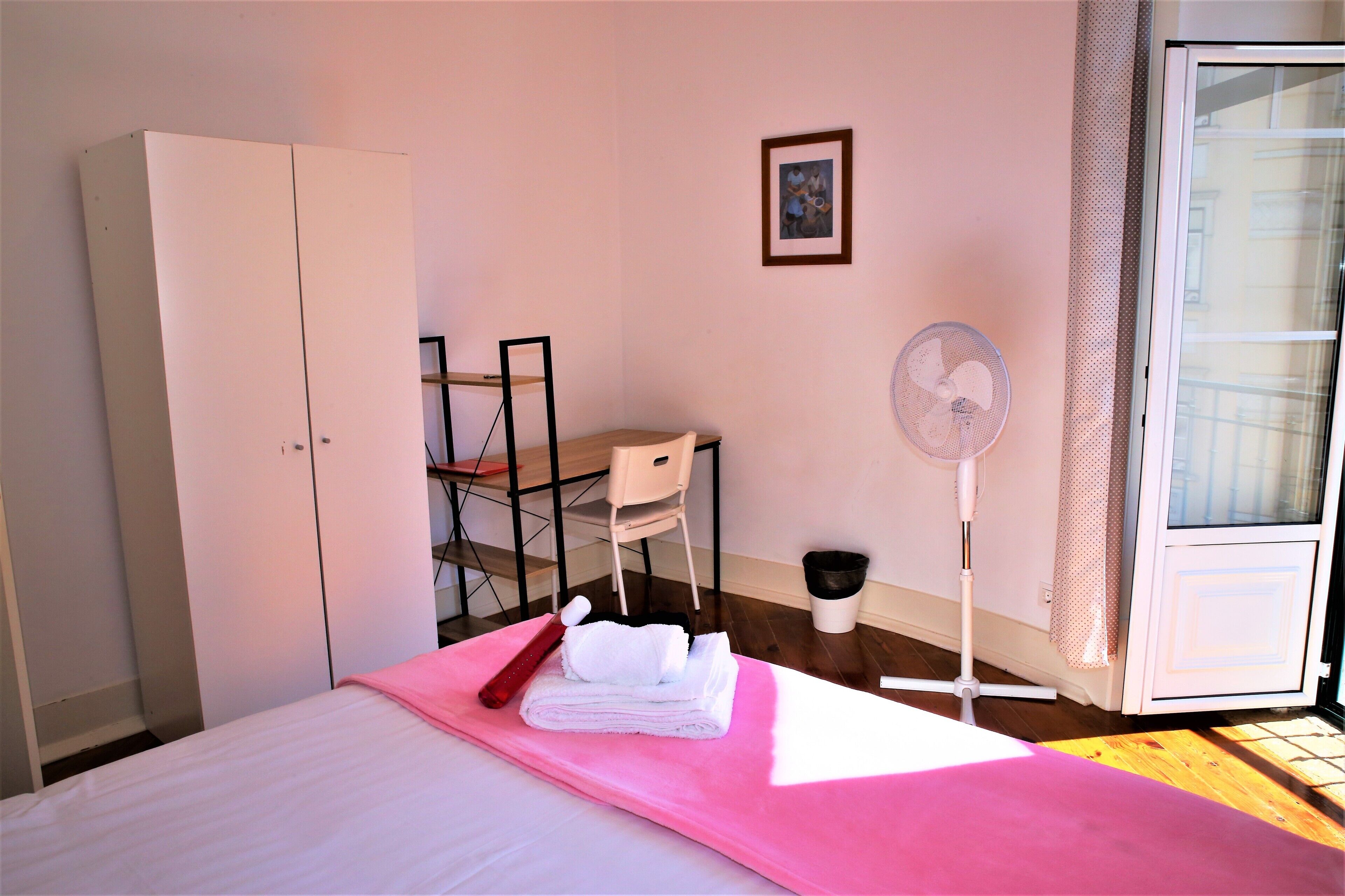 Un dormitorio con cama, un armario blanco, una silla, un ventilador y un cuadro en la pared.