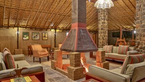 A cozy lounge area with sofas, a fireplace, and a stone pillar. - The Untamed Bandhavgarh by TUTC (Manpur)
