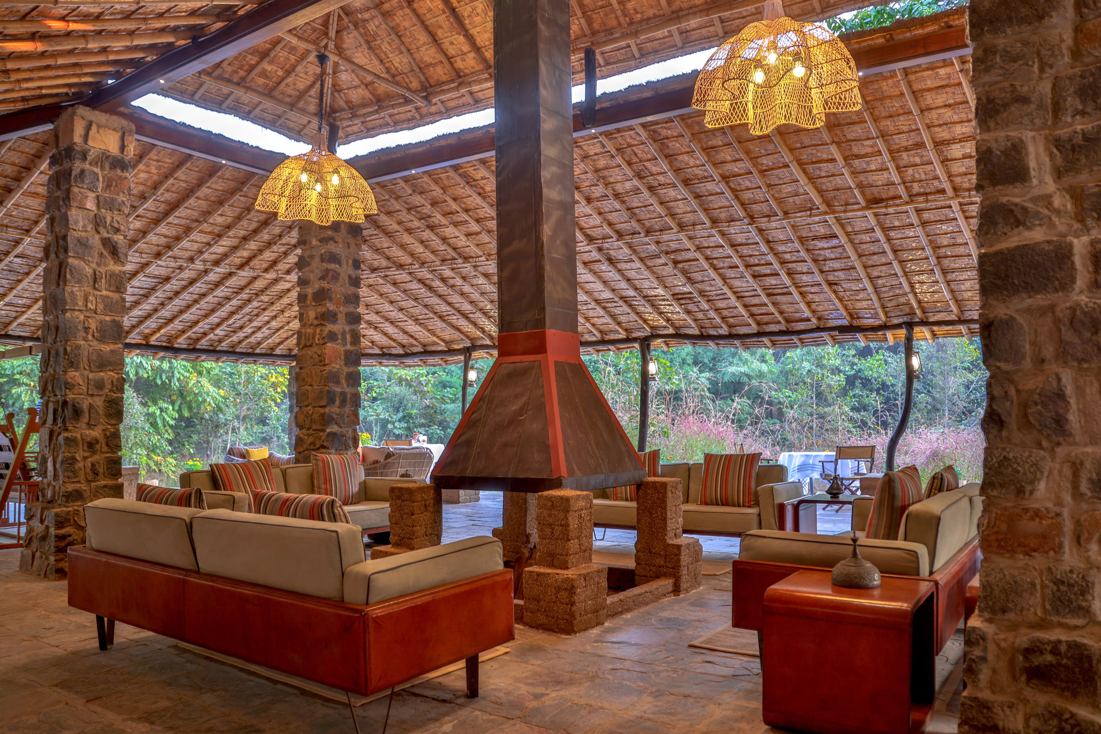 A covered outdoor seating area with stone pillars, cushioned sofas, and hanging light fixtures.