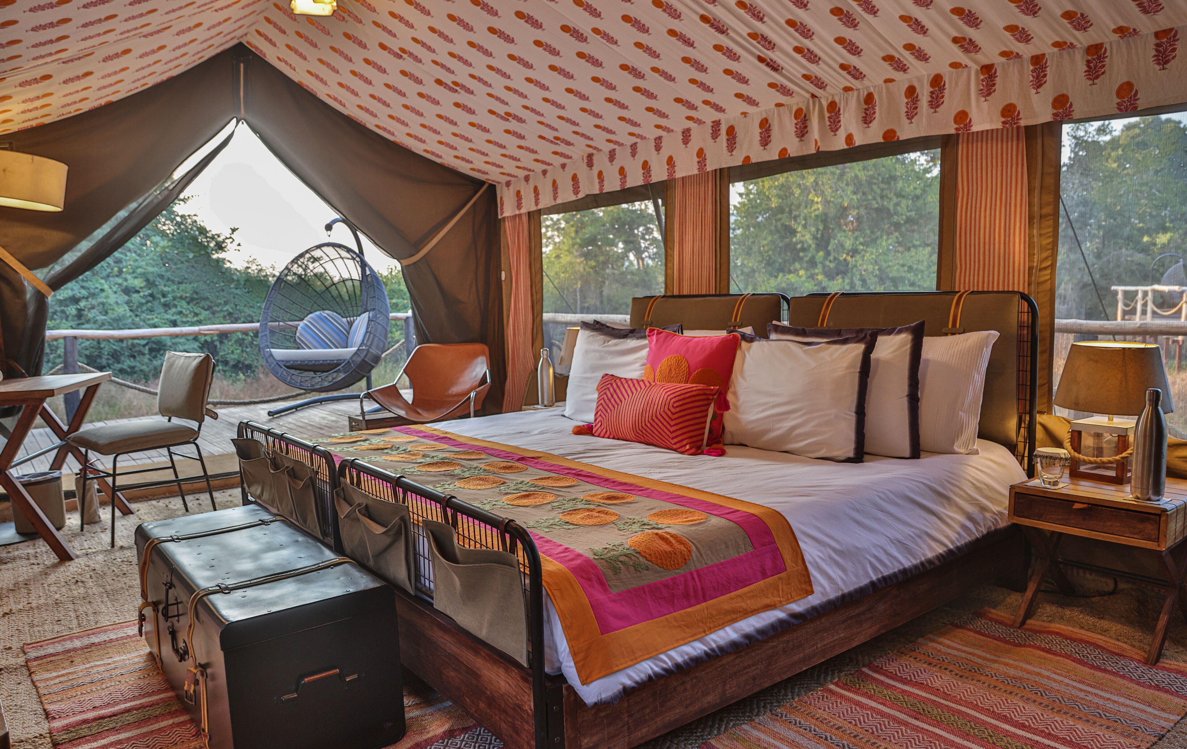 A spacious bedroom with a large bed, a wooden headboard, a hanging chair, and a small table with a lamp.