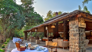 An outdoor dining area with a stone pillar labeled "Gaze," wicker furniture, and a table set with plates and cups. - The Untamed Bandhavgarh by TUTC (Manpur)