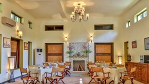 A spacious dining area with high ceilings, a central fireplace, and multiple tables set for dining. - The Untamed Bandhavgarh by TUTC (Manpur)