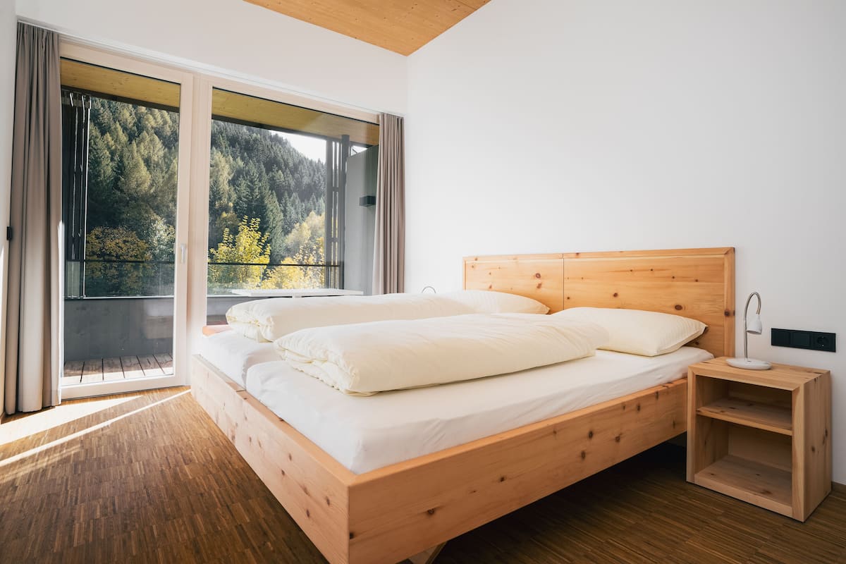 Un dormitorio con una cama de madera, una mesita de noche y un ventanal con vistas a árboles.