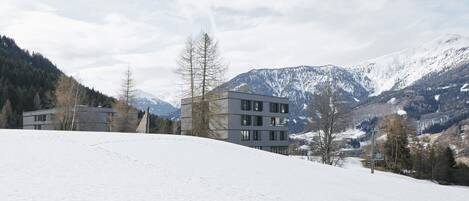Un edificio moderno con varios pisos, rodeado por un paisaje nevado y montañas al fondo.