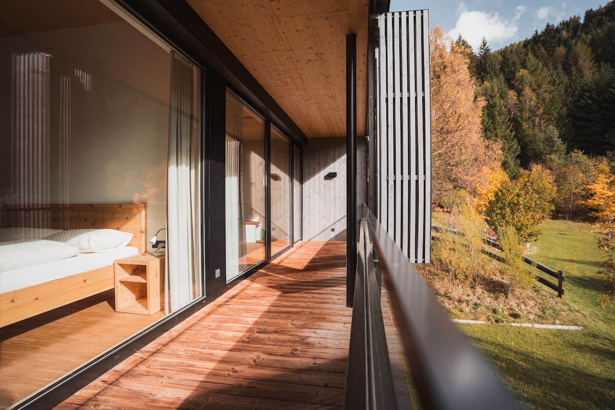 Un dormitorio moderno con suelo de madera, ventanas amplias y vistas a una zona boscosa.