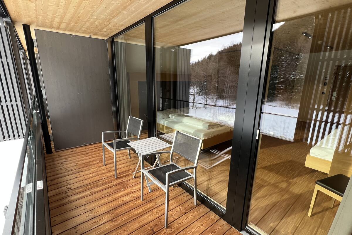 Una habitación moderna con suelo de madera, pared de cristal y cama con vistas a un paisaje nevado.