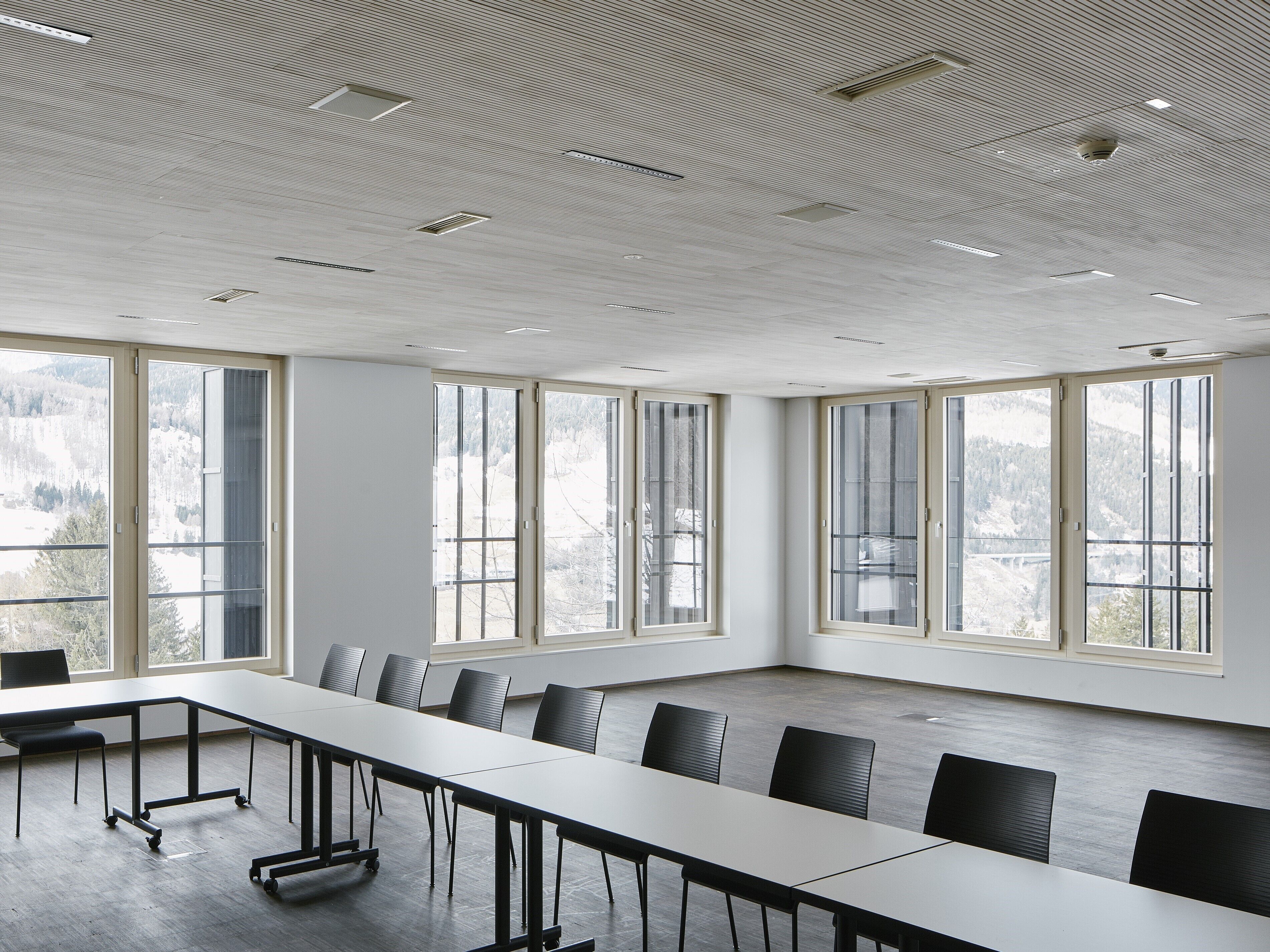Ein Konferenzraum mit langem Tisch, schwarzen Stühlen und großen Fenstern mit Blick auf eine verschneite Landschaft.