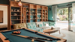 A pool table with pool balls, a sofa, and a bar area with shelves labeled "BAR," "WELCOME," "HOME," and "SUMMER."