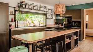 A modern kitchen with a central island, bar stools, and a hanging light fixture.