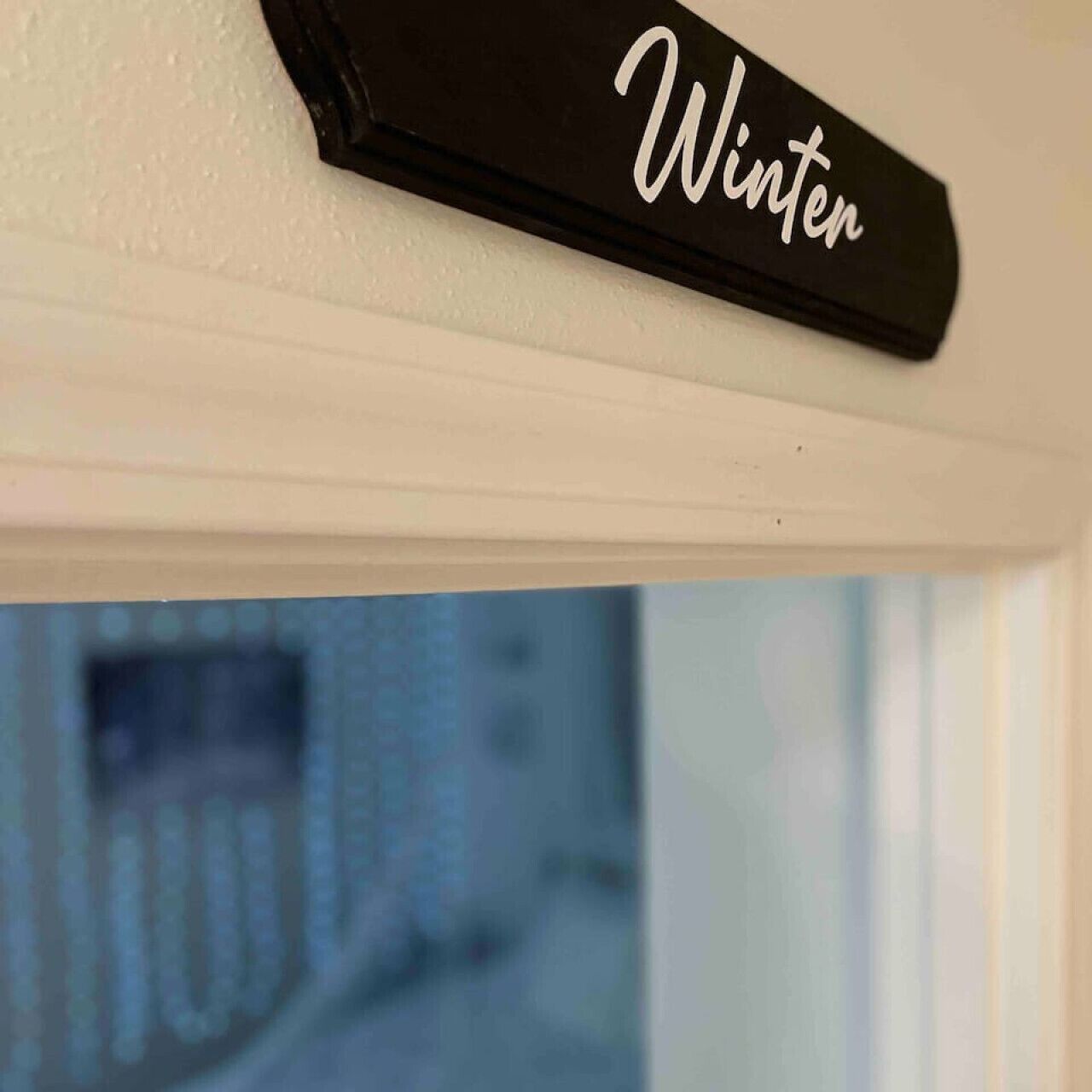 Ein schwarzes Schild mit dem Wort "Winter" an einer weißen Wand.