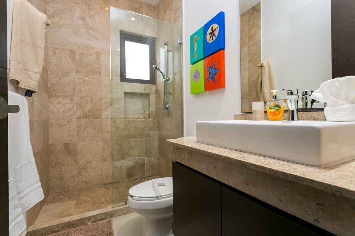 A modern bathroom with a glass-enclosed shower, a white toilet, and a sink with a marble countertop.