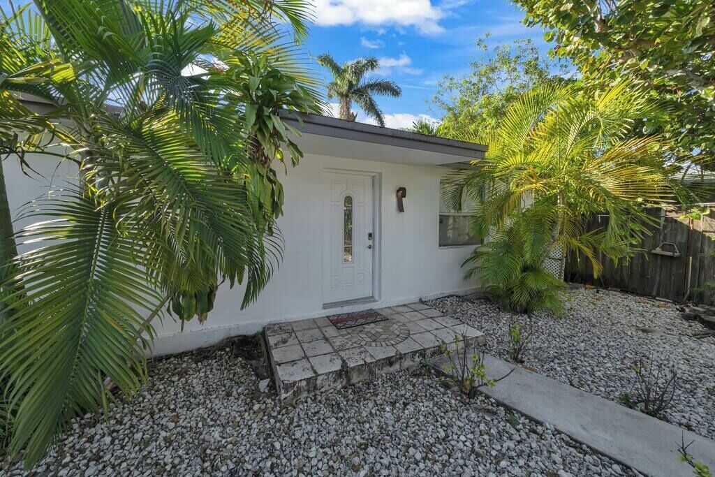 A small, single-story house with a white exterior, a front door, and a small porch area.