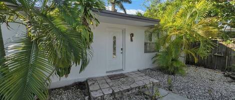 A small, single-story house with a white exterior, a front door, and a small porch area.