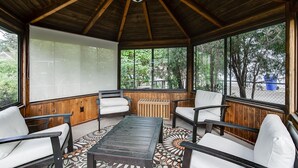 A covered patio area with wooden flooring, a central table, and four chairs. - Charming Mid-Century Modern Eco-Friendly Home (Saint Paul)