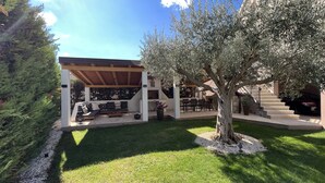 A covered outdoor seating area with a built-in grill, a stone staircase, and a large tree. - Romantic vacation apartment with large pool and beautiful garden (Bale)