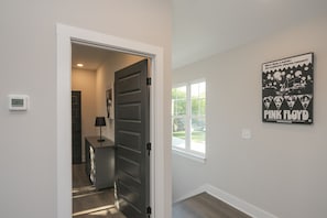 A hallway with a door leading to a room, a thermostat, a window with a view, and a Pink Floyd poster on the wall.