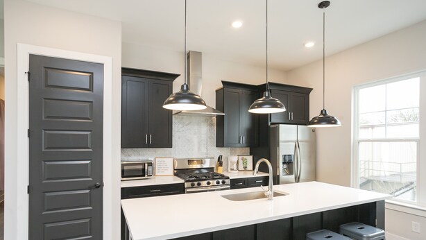 Cocina moderna con armarios oscuros, encimera blanca, una isla central con taburetes e iluminación colgante.
