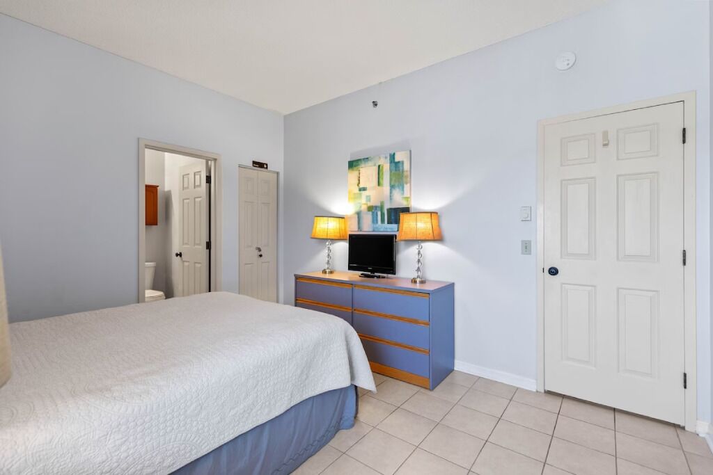 A bedroom with a bed, a dresser with a TV, and a door.