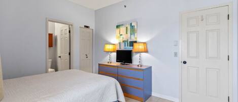 A bedroom with a bed, a dresser with a TV, and a door.