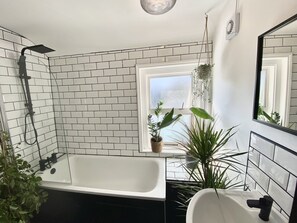 Ein modernes Badezimmer mit einer freistehenden Badewanne, einem weißen Waschbecken und einem Fenster mit Pflanzen.