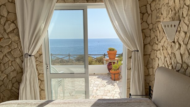 A bedroom with a view of the sea, stone walls, and a balcony with potted plants. - Carvoeiro Sol Right by the sea (Carvoeiro)
